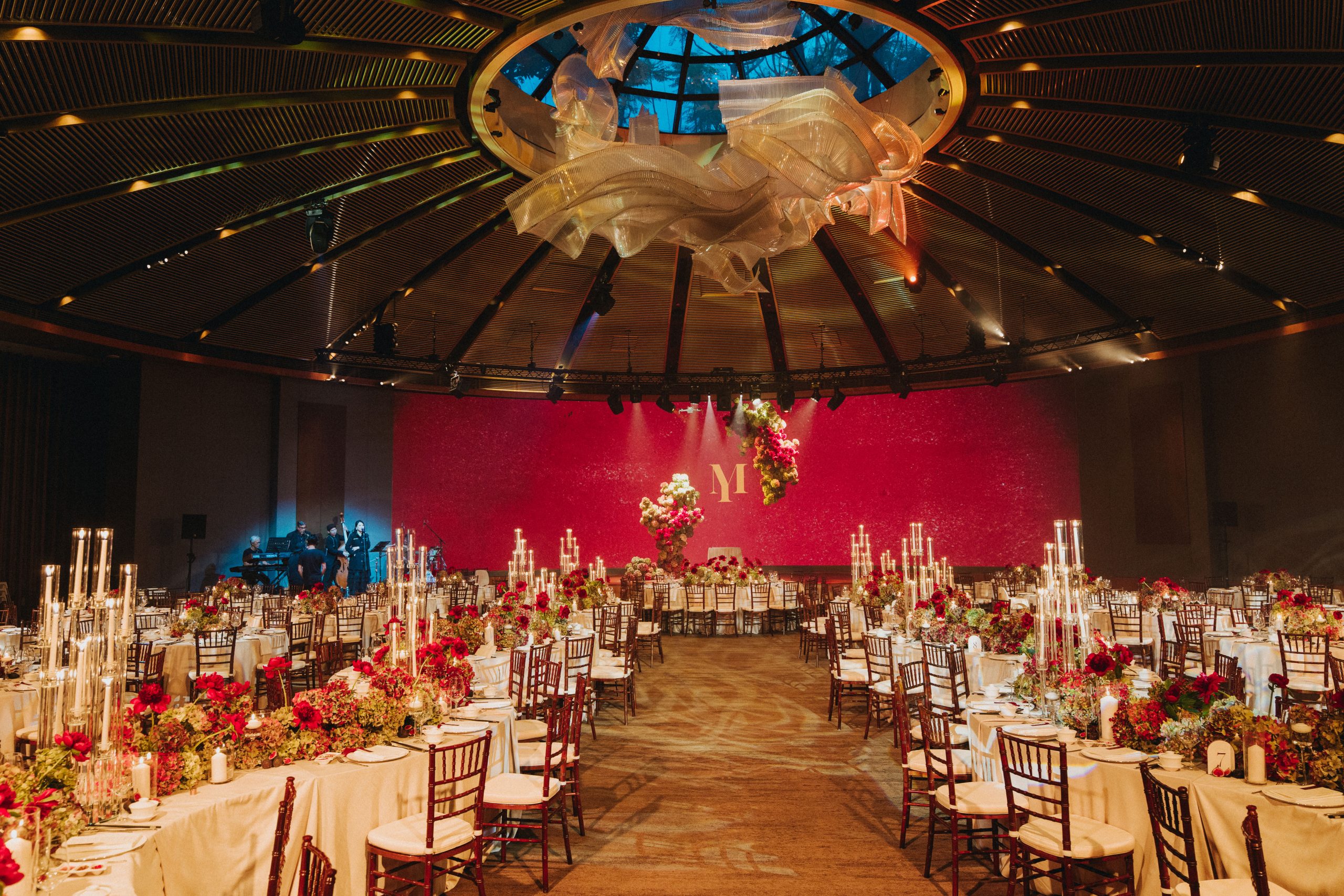Luxury wedding reception with grand ballroom setup, red floral décor, and elegant candlelit tables