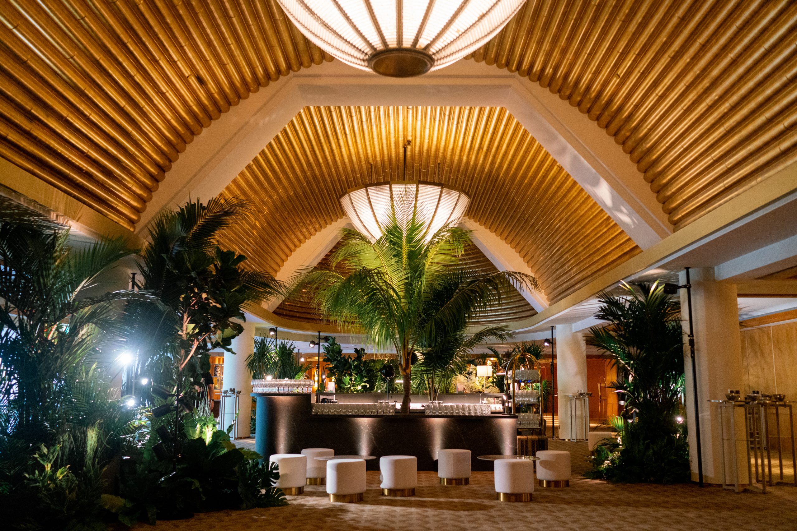Luxury indoor event space with tropical decor, golden ceiling design, and central bar setup