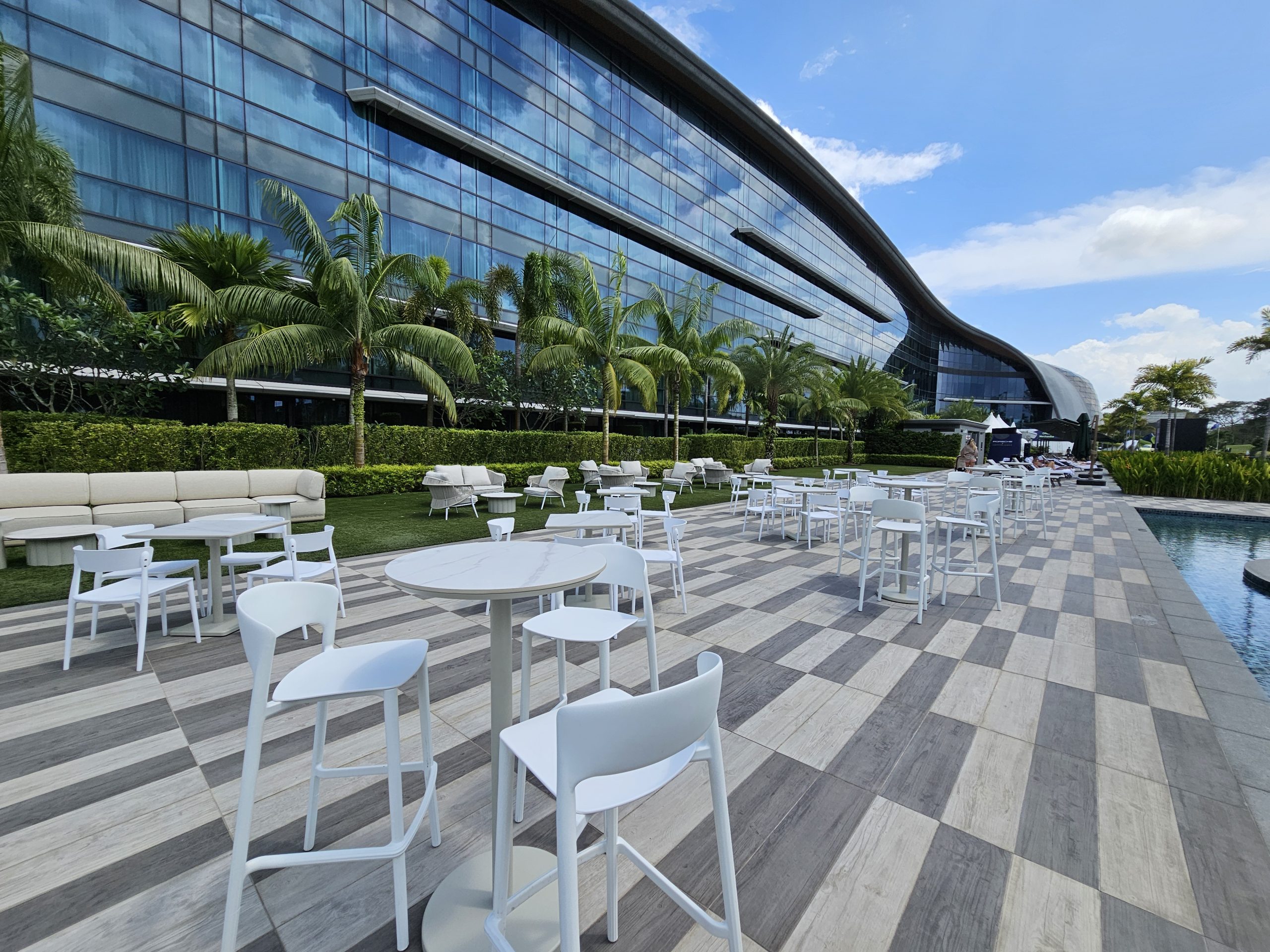 Outdoor corporate event setup with white seating, poolside venue, and modern glass building backdrop