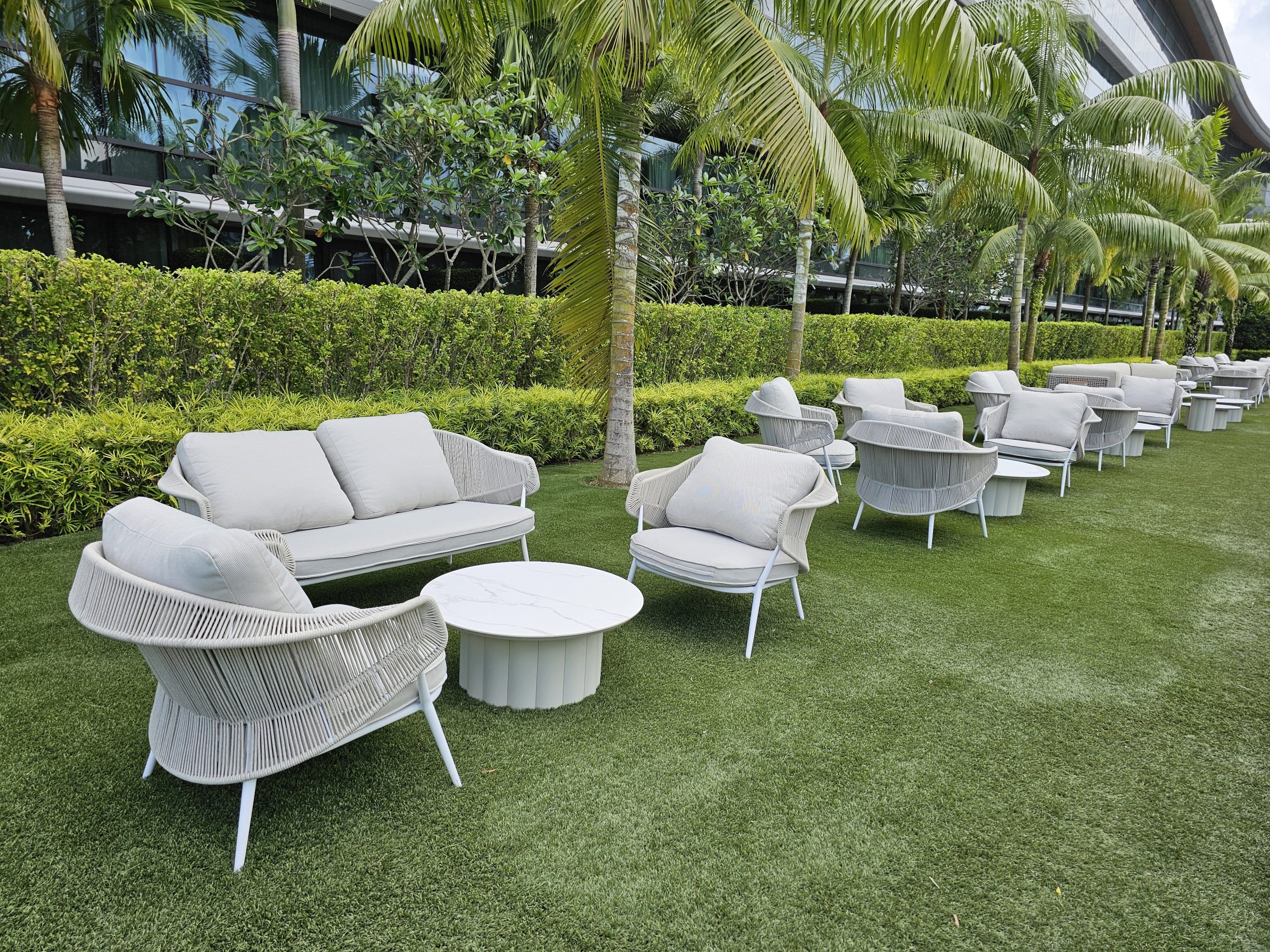 Luxury outdoor lounge seating setup with modern furniture on lawn surrounded by palm trees and greenery