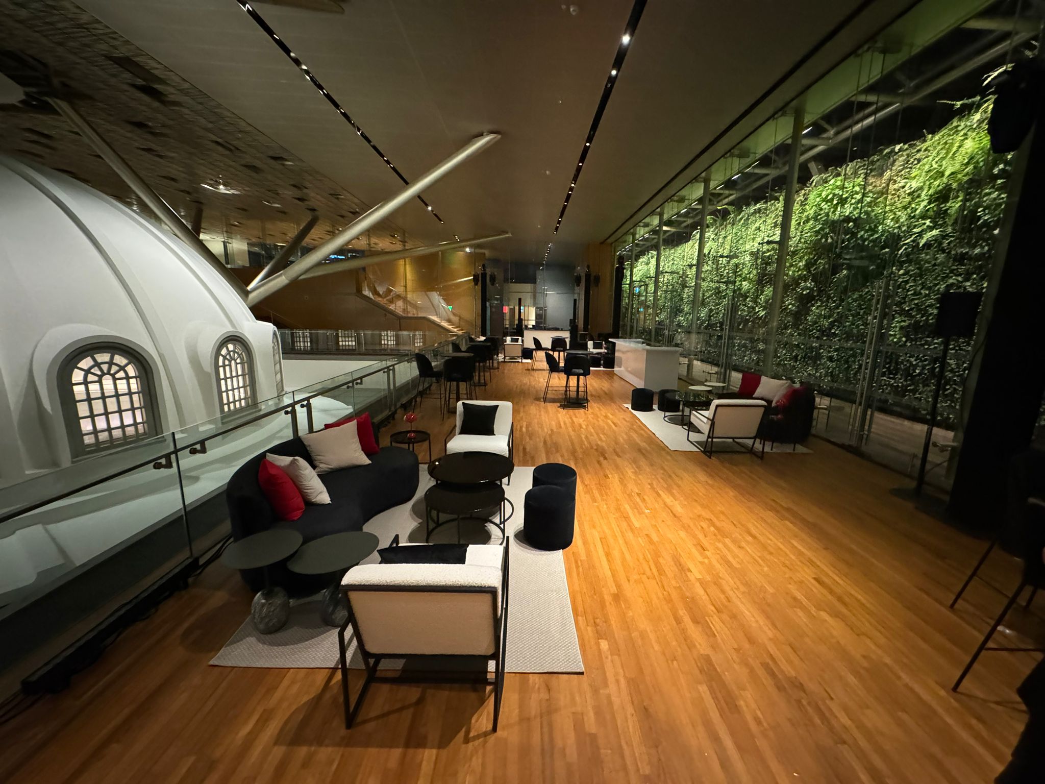 Modern indoor event lounge setup with designer seating, wooden flooring, and glass wall with vertical greenery
