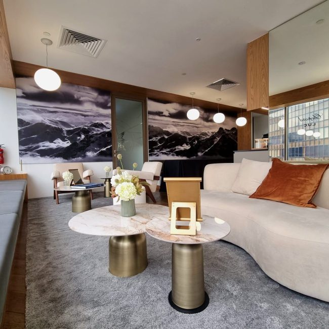 Modern luxury lounge with curved sofa, marble tables, pendant lighting, and mountain wall art in a stylish corporate setting