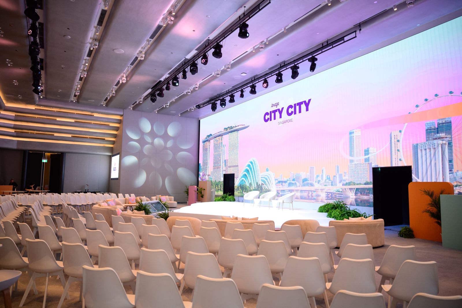 Modern corporate event stage with large LED screen, conference seating, and professional lighting setup