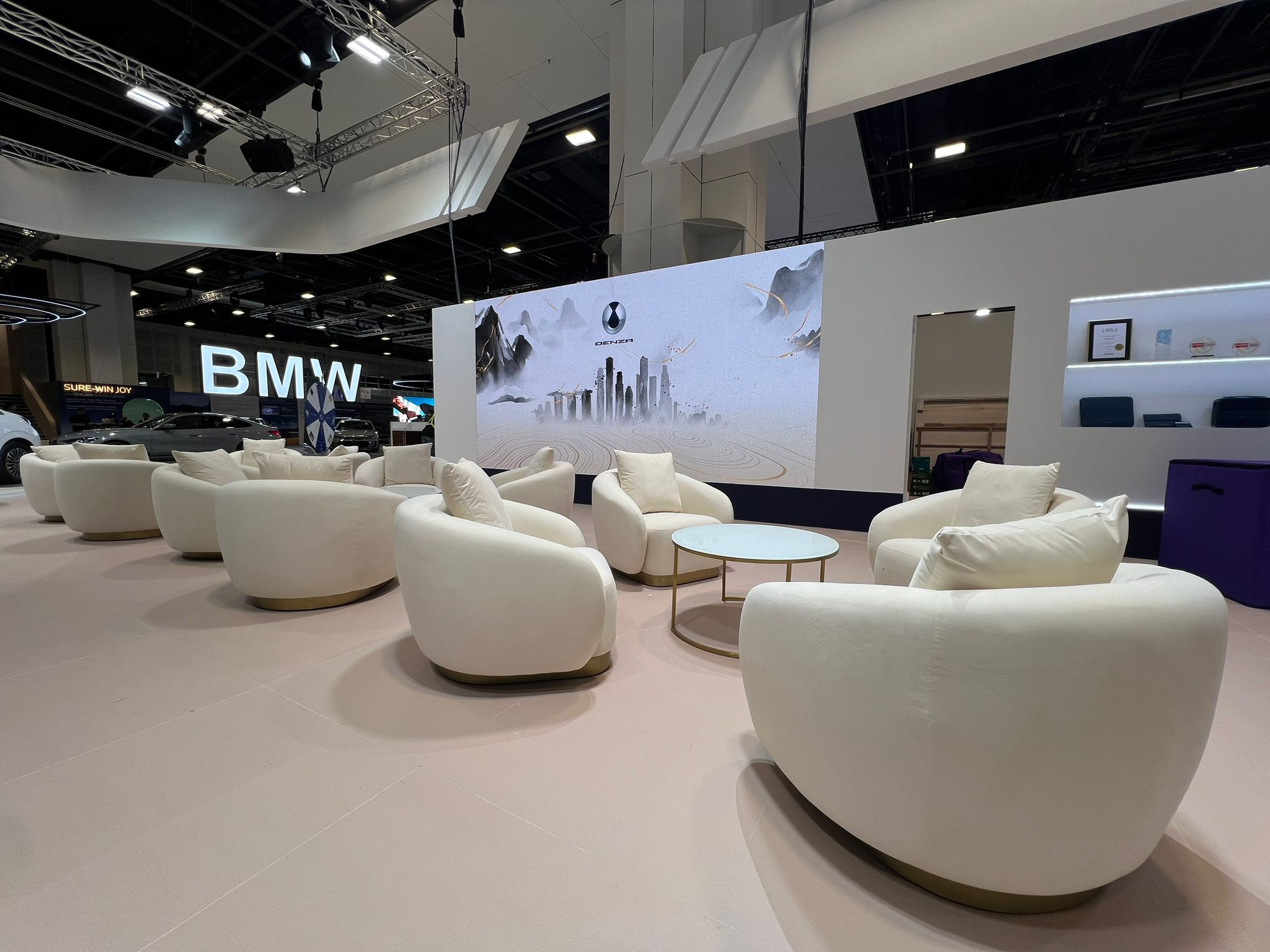 Modern exhibition lounge with white designer seating at an automotive trade show booth featuring BMW branding