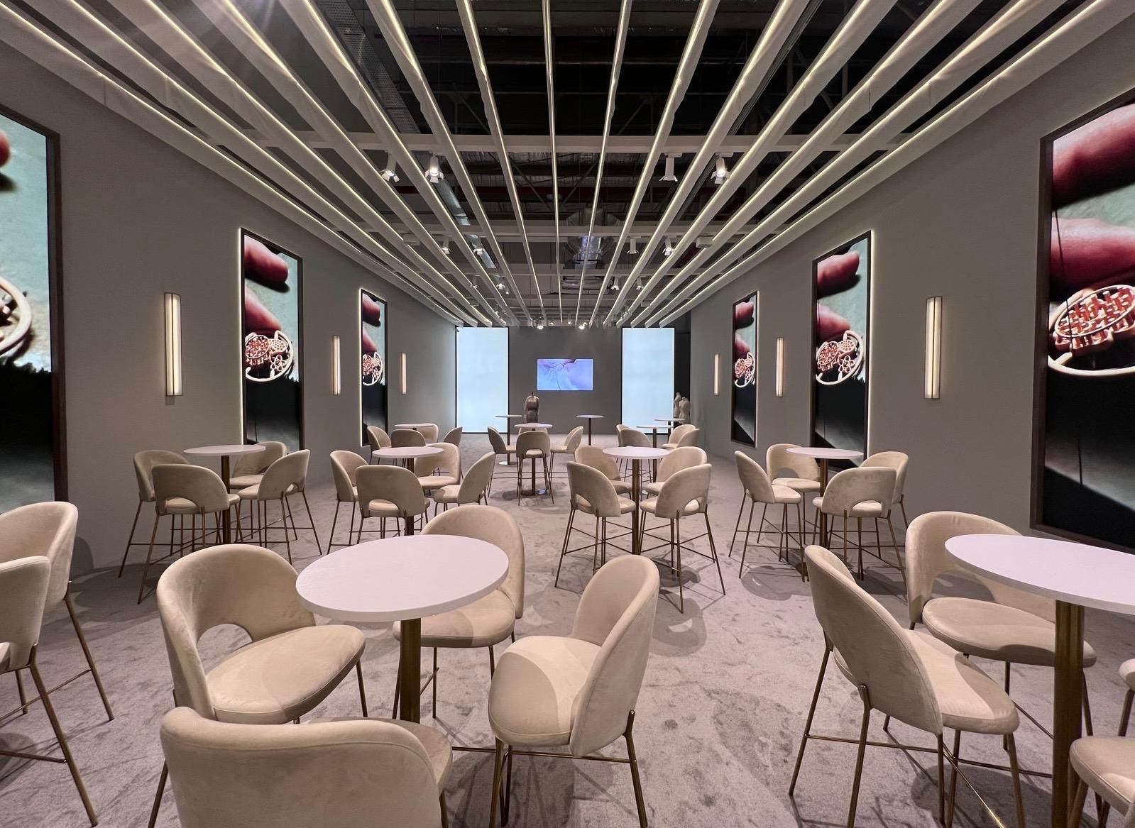 Modern exhibition lounge setup with minimalist seating, ambient lighting, and luxury brand display panels