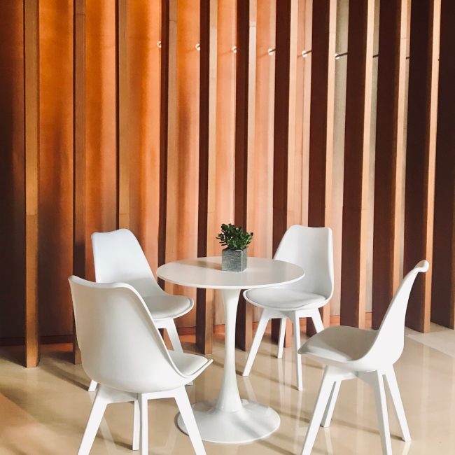 Minimalist seating area with white chairs and round table against a warm wooden panel wall
