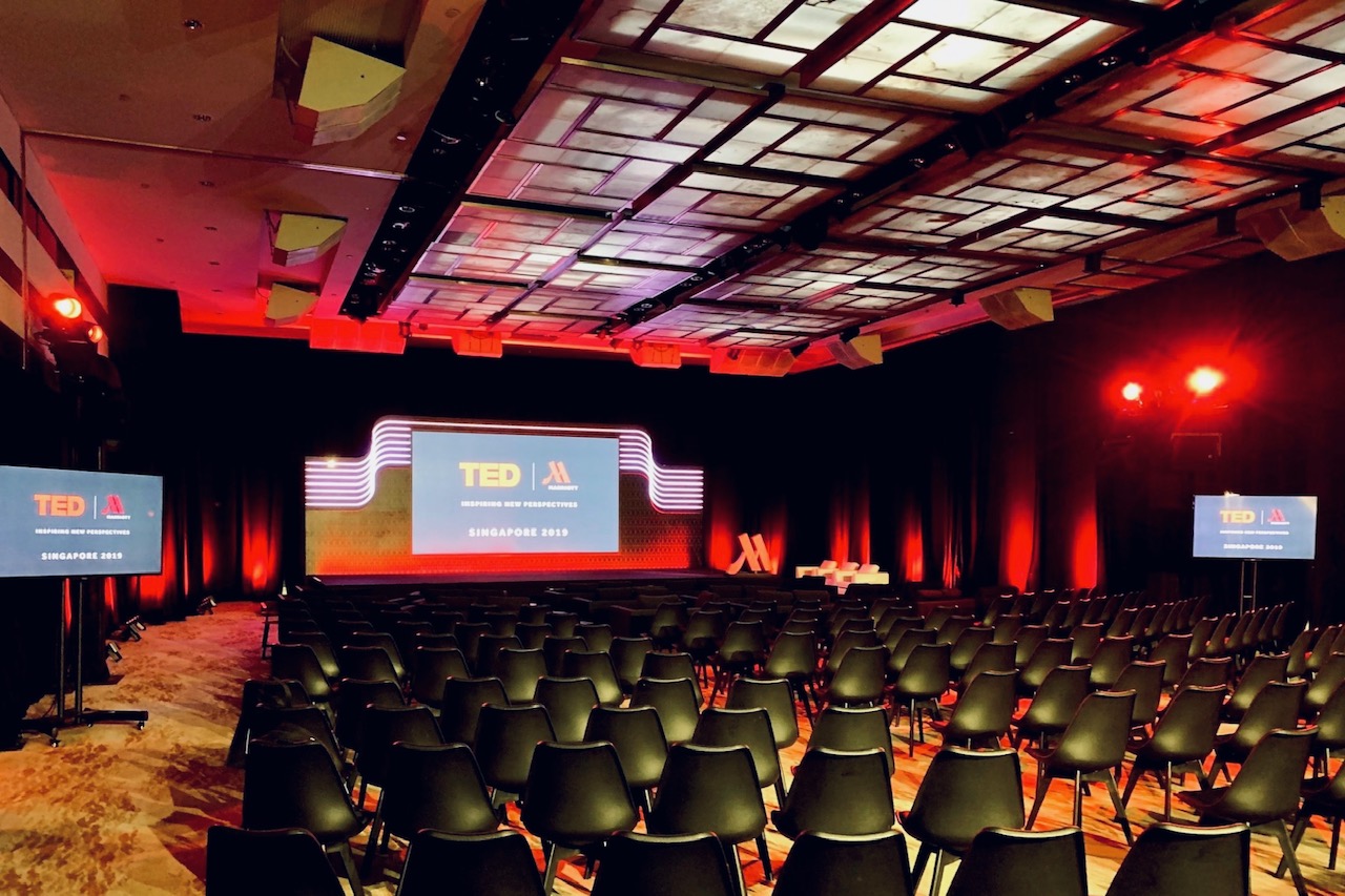 Conference event setup with stage, large screen display, and auditorium seating with lighting design