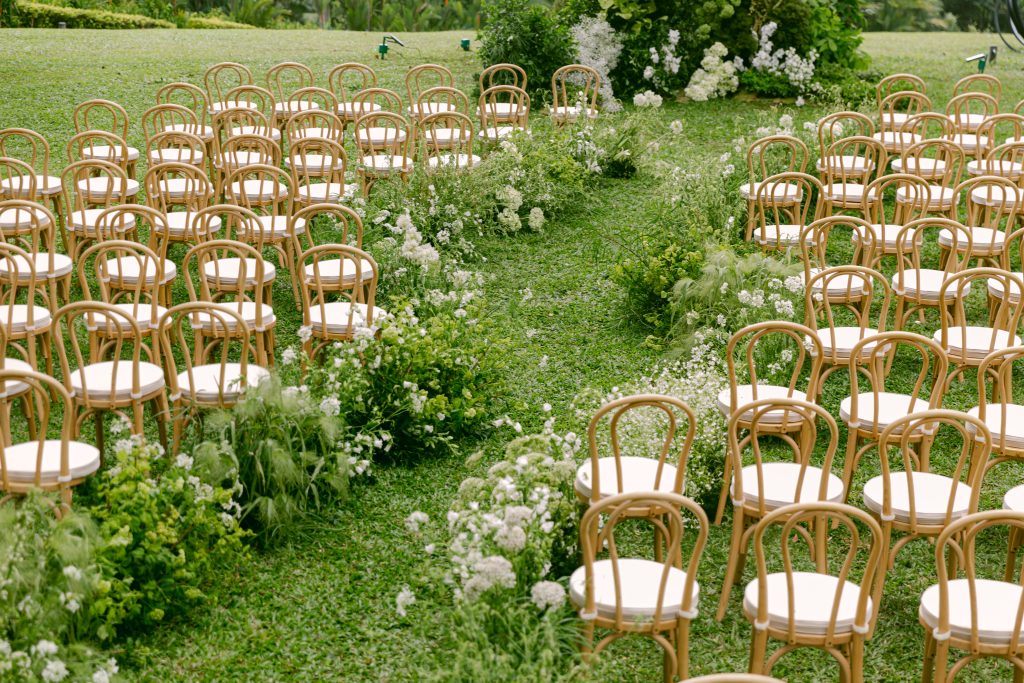 Outdoor garden wedding ceremony aisle with wooden chairs and natural floral arrangements