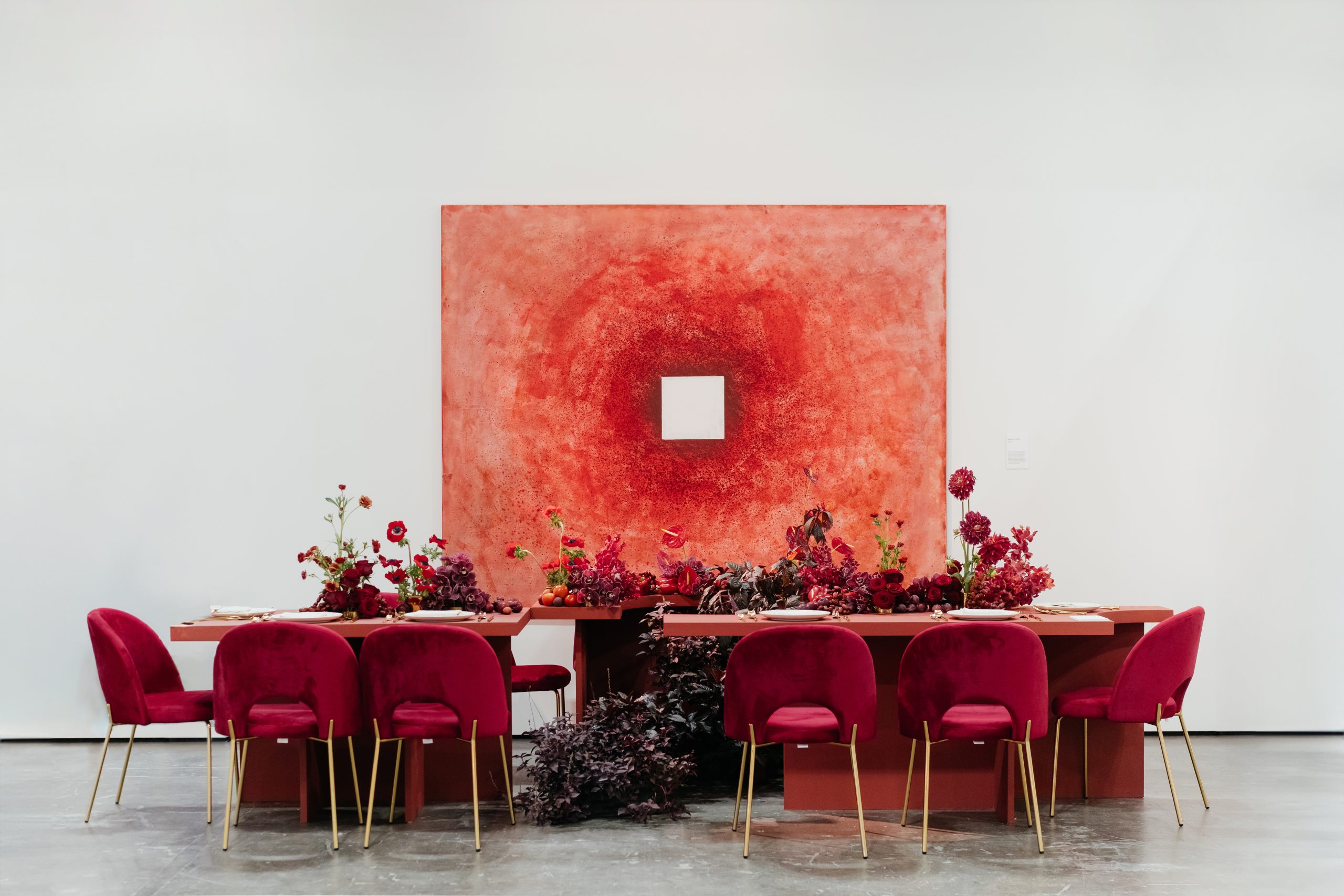 Luxury dining setup with red theme décor, velvet chairs, floral arrangement, and modern art backdrop