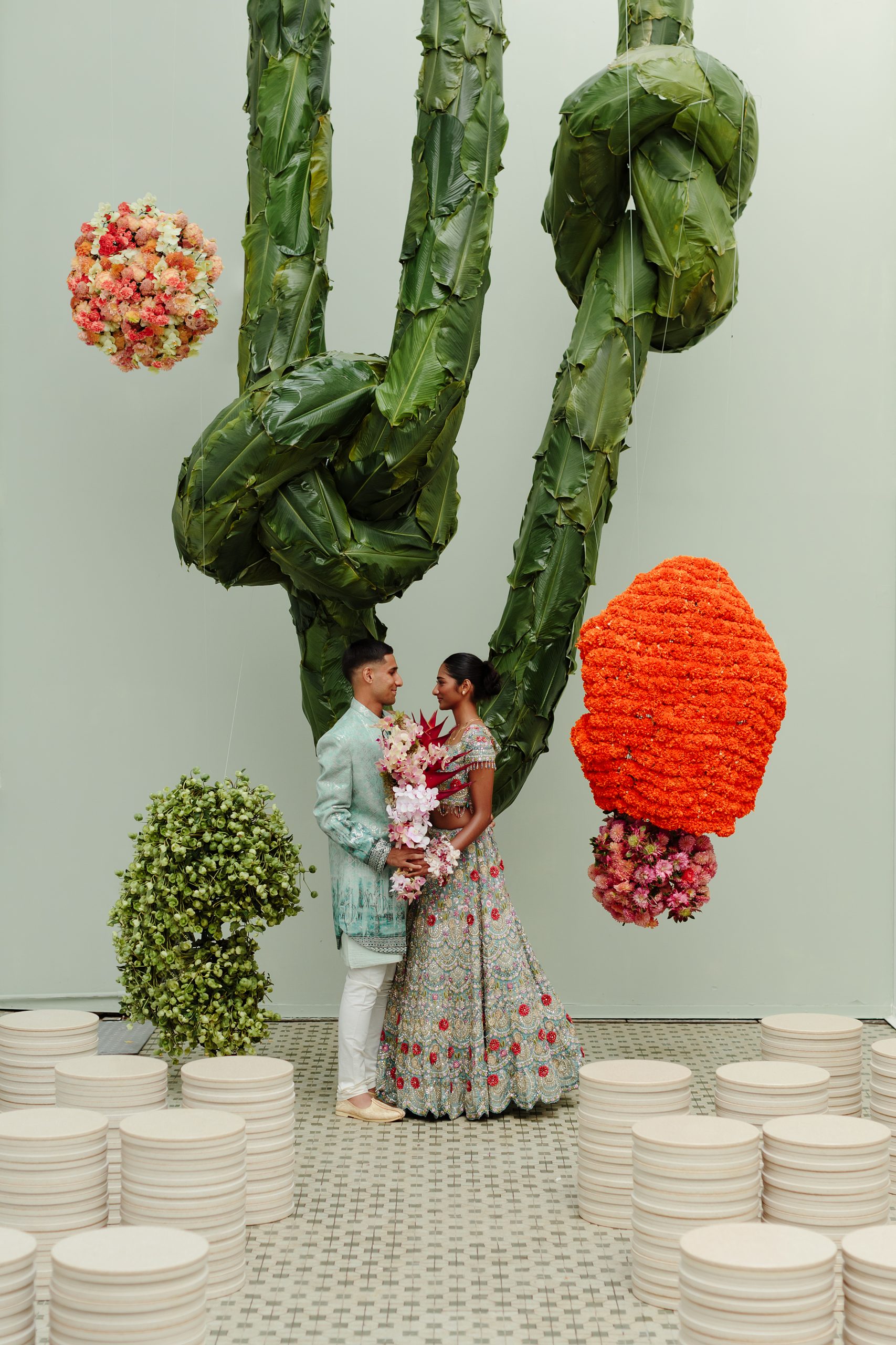 Indian wedding couple in traditional attire with floral installation and modern artistic décor backdrop